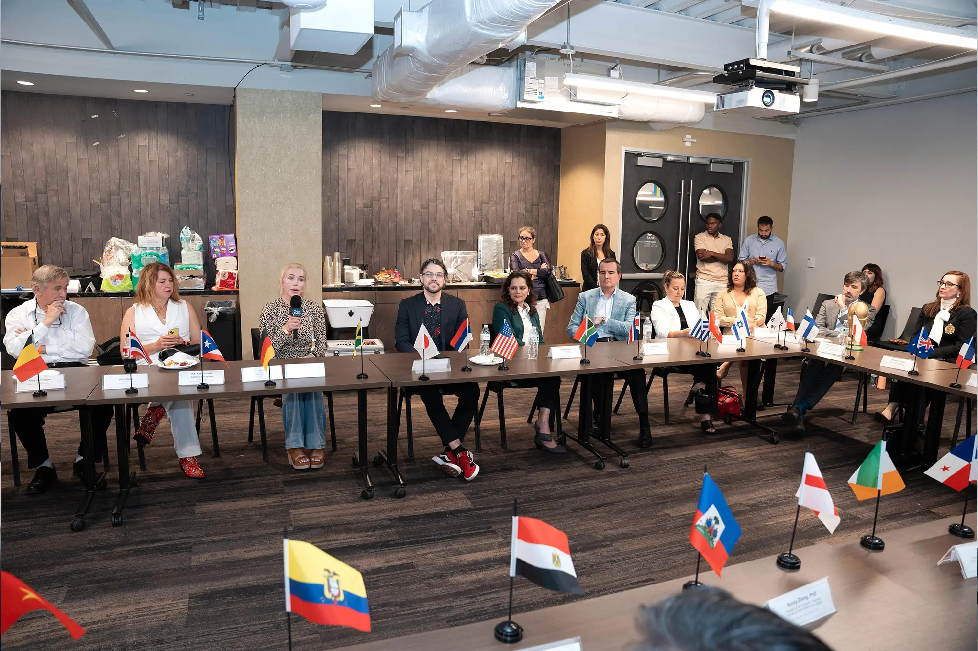 A boardroom table set with flags and people seated around it
